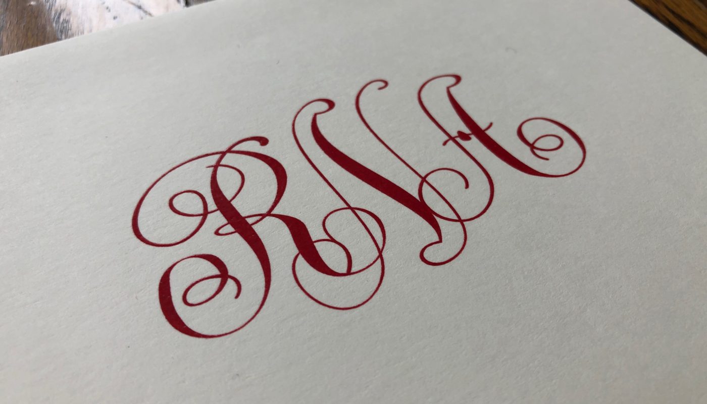 This is an image of a monogram on a folded note. The lettering is printed in red ink and it's on white paper